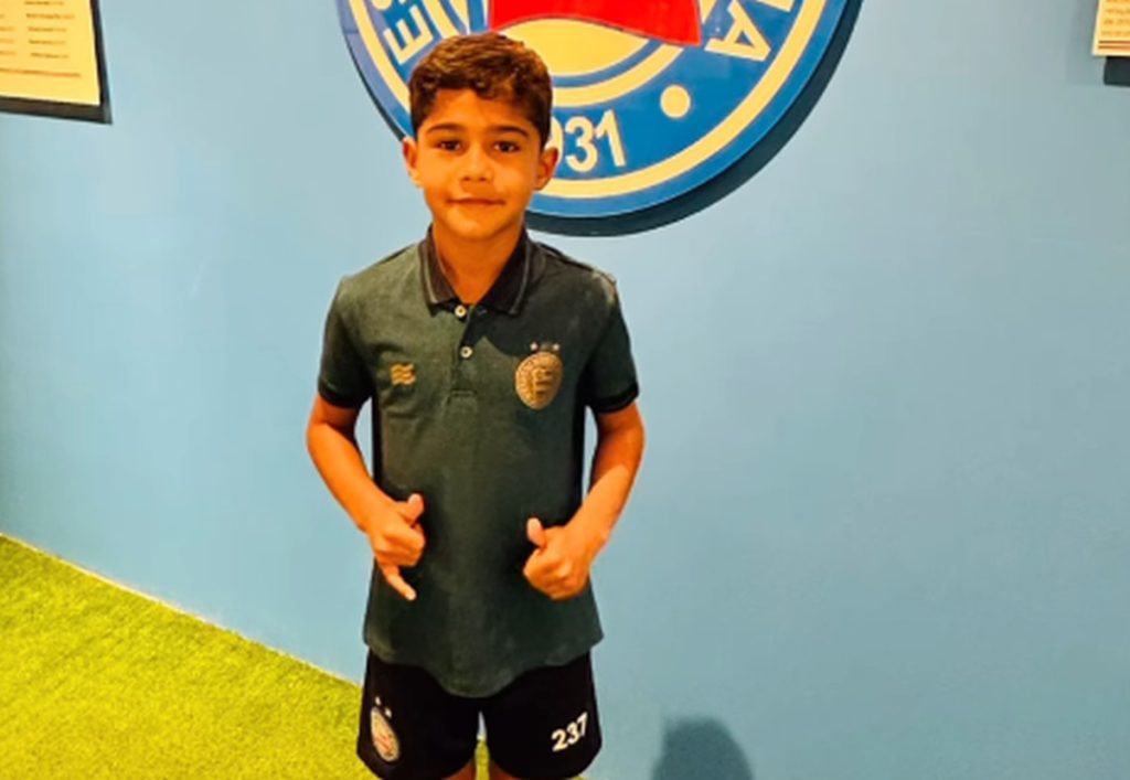 Jovem jogador do Bahia, Alexandre, de 7 anos, aparece em foto com o escudo do Bahia ao fundo